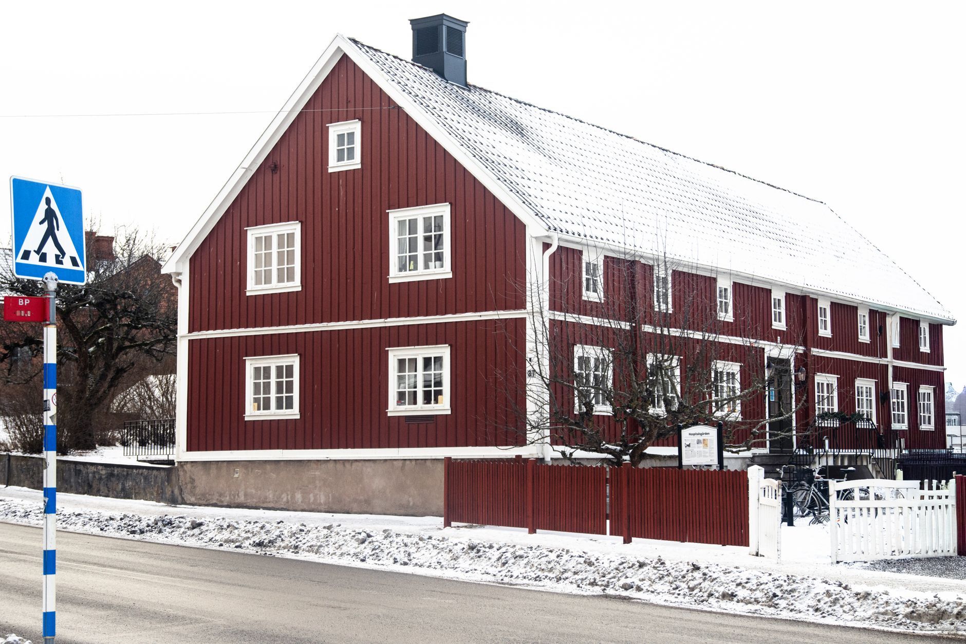 Rødt trehus med snø på taket langs en vintergate