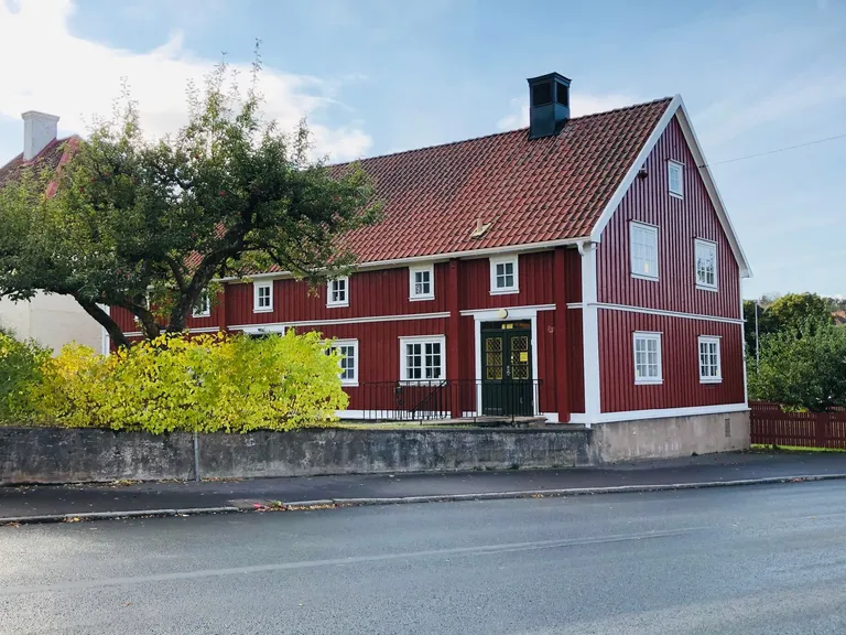 Rødt trehus med hvite vinduskarmer bak en lav mur og et tre