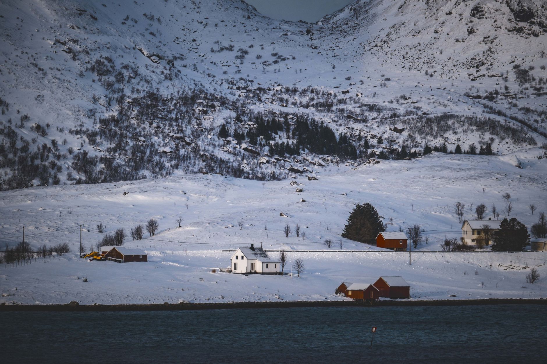 Små trehus i snødekt landskap ved en fjord, med fjell bak