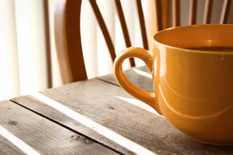 Gul kaffekopp på et trebord i morgenlys fra vinduet bak