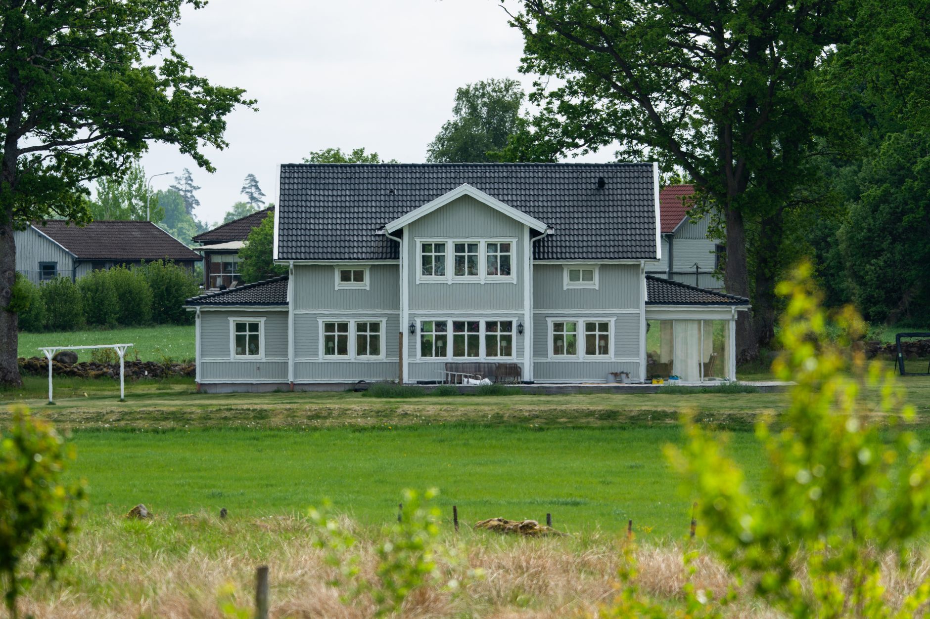 Lys enebolig med mørkt tak sett over en gresslette i dagslys