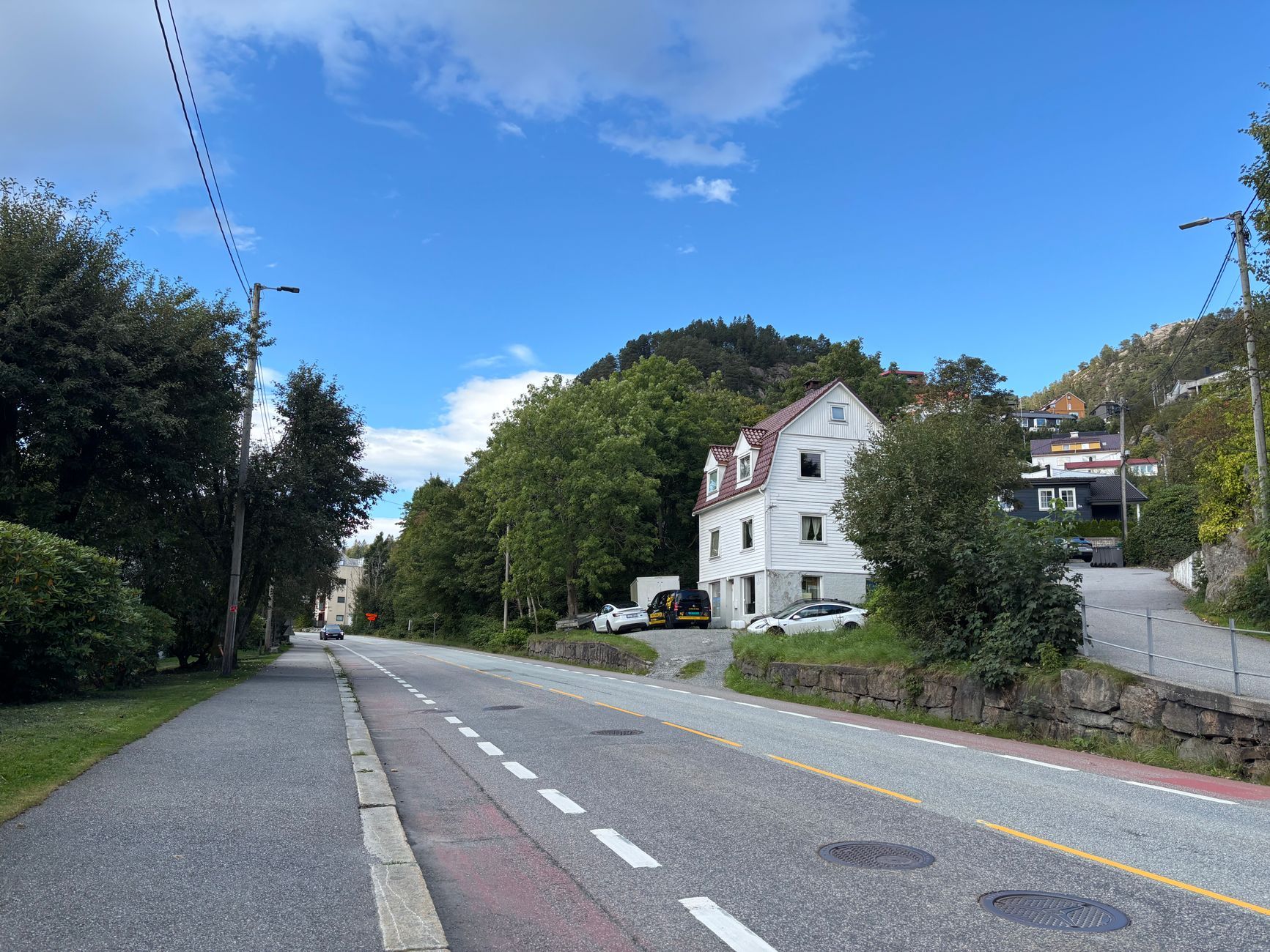 Hvitt trehus langs en rolig boligvei i Norge en sommerdag