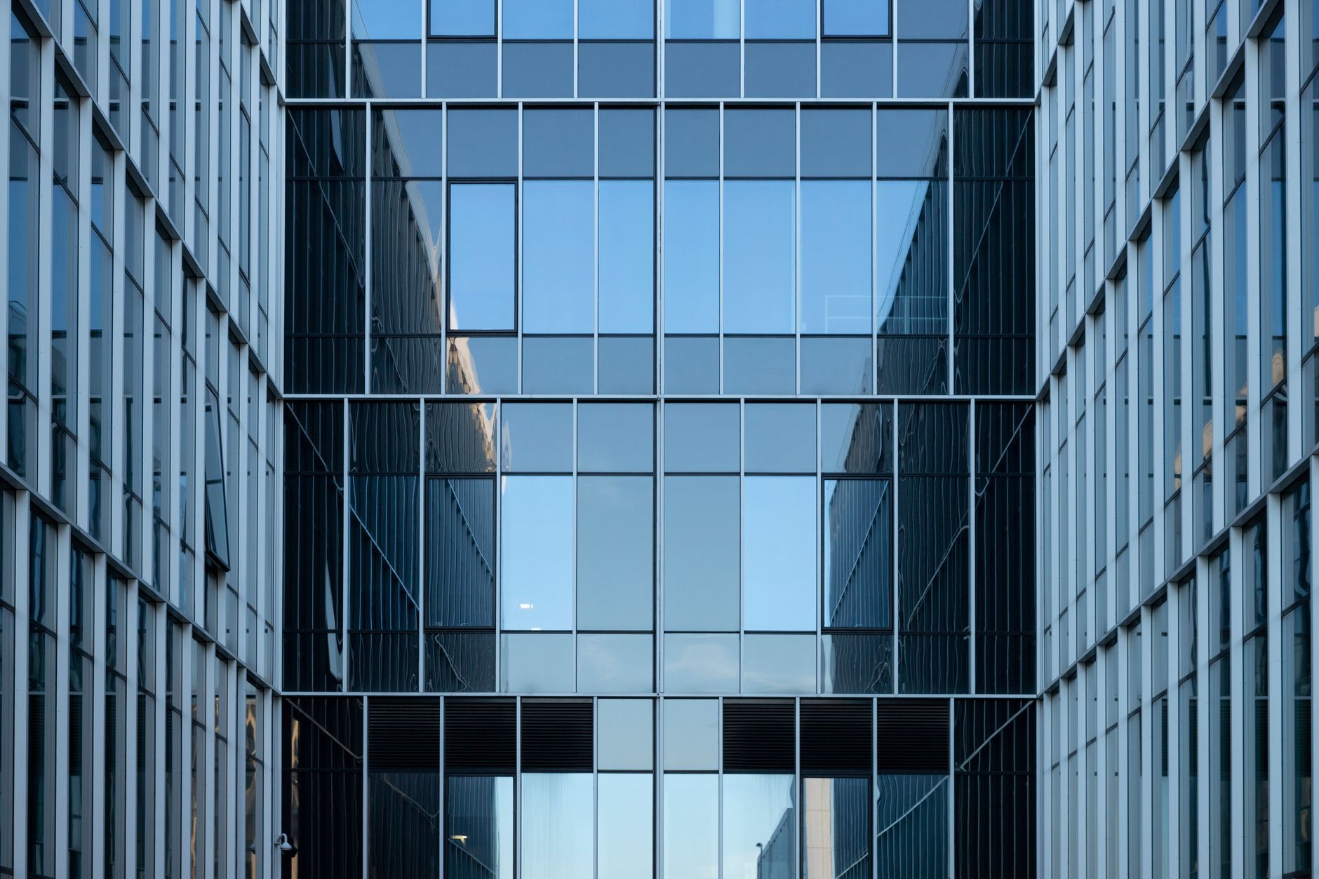 Symmetrisk glassfasade på moderne kontorbygg mot grå himmel