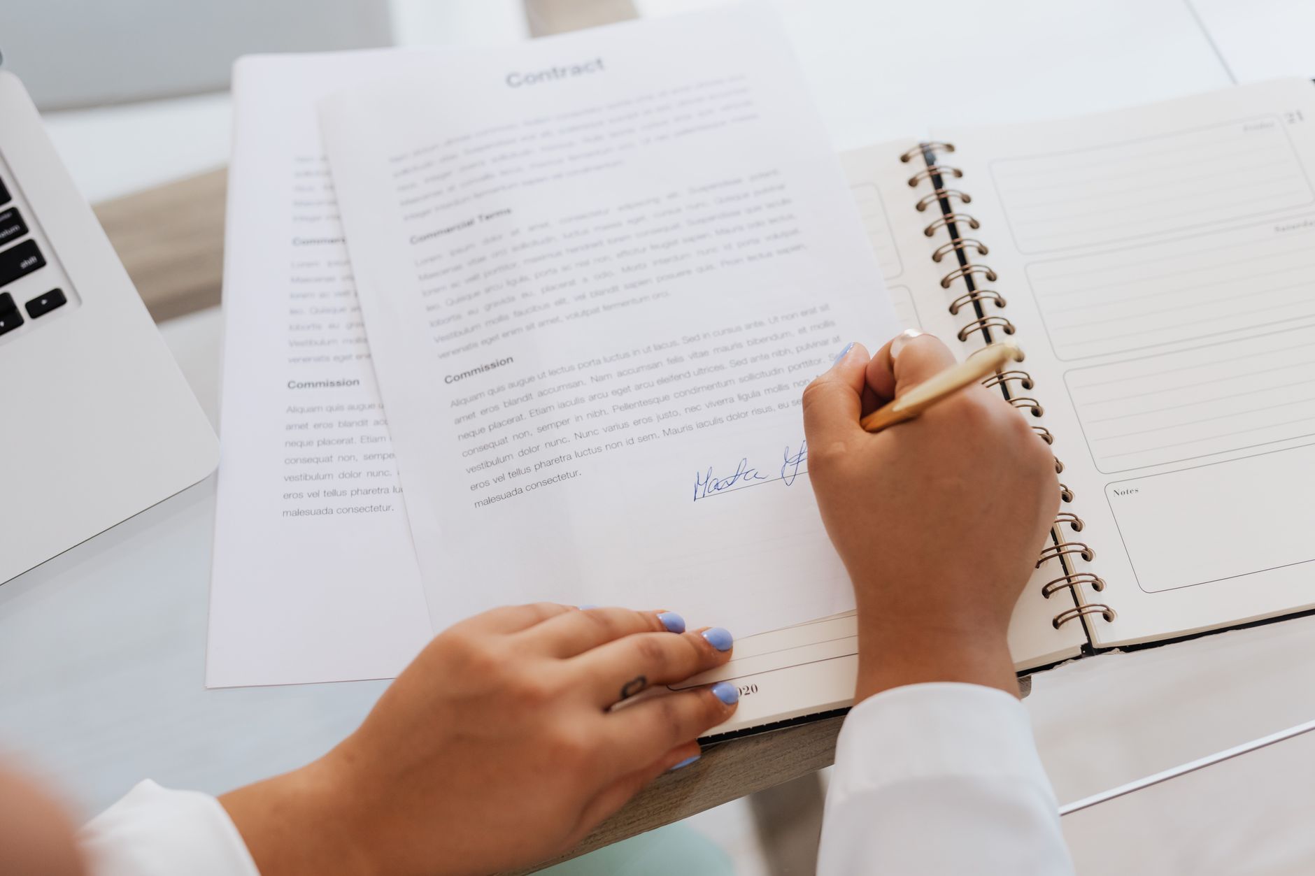 Hender som signerer et dokument med penn ved et lyst skrivebord